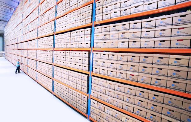 A well-organized warehouse with neatly stacked boxes and a worker using a tablet to manage inventory, illustrating efficient product storage and streamlined logistics for shipment to Amazon fulfillment centers